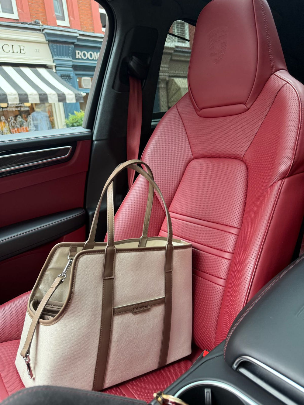 Beige handbag on a red car seat with a city street view outside